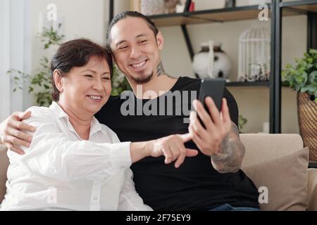 Heureux beau homme de race mixte demandant à la mère mature de prendre le selfie avec lui Banque D'Images