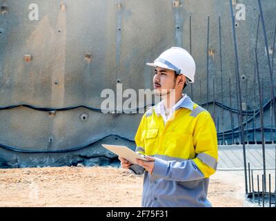 Jeune, belle ingénierie de tunnel asiatique portant une veste haute visibilité et casque de sécurité blanc fonctionnant et utilisant une tablette numérique au tunnel construction Banque D'Images