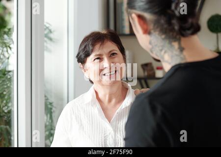 Bonne femme mûre souriante de race mixte regardant le fils adulte visiter elle à la maison Banque D'Images