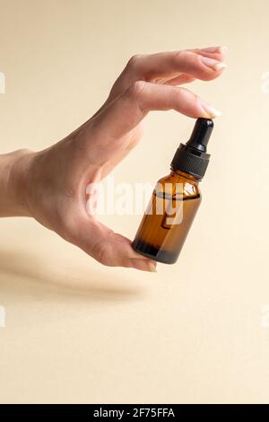 Main femelle avec Dropper d'huile essentielle, d'essence d'aromathérapie, de sérum de beauté ou de liquide médicinal sur fond beige. Flacons sans marque pour votre desig Banque D'Images
