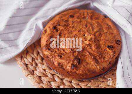 Gâteau rond au lait caillé avec raisins secs enveloppés dans une serviette de cuisine blanche sur un support en osier. Banque D'Images