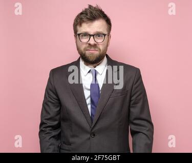 Homme fatigué et délabré dans un costume d'affaires stressé, il n'a pas pu conclure une affaire et très contrarié. Fond rose. Banque D'Images