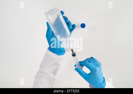 Une vue de dessus d'une main gantée dessine une solution pour le traitement des rhumes et des virus à partir d'un flacon avec une seringue. Banque D'Images