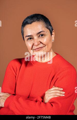 Photo de la femme smiley aux cheveux gris courts posant en studio sur fond marron. Banque D'Images