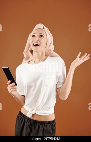 Bonne heureuse jeune femme excitée de recevoir un message texte avec de grandes nouvelles lors de la vérification du téléphone après la douche du matin Banque D'Images