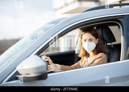 Jeune femme conduisant une voiture avec un masque de protection sur son visage. Je m'inquiète de l'appareil photo. Santé, protection contre les virus, concept de protection contre les allergies. Banque D'Images