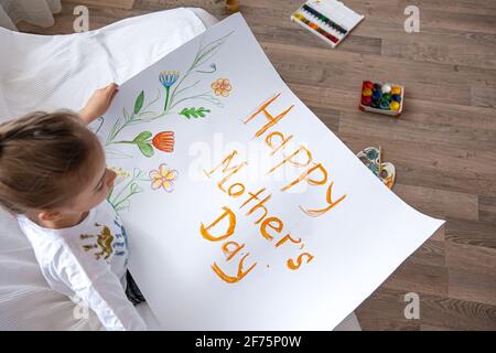 Une petite fille peint une carte de vœux pour maman le jour de la fête des mères avec l'inscription Happy Male's Day. Banque D'Images