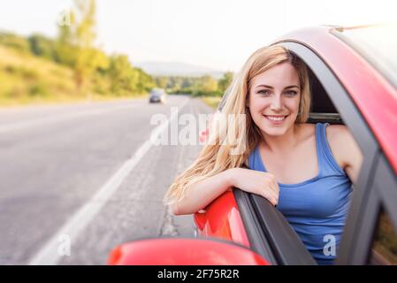 Une femme heureuse et belle conduit une voiture rouge. Banque D'Images