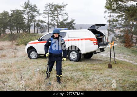 Un homme en costume spécial travaille avec un détecteur de métal, à la recherche d'un dispositif explosif. Banque D'Images