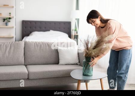 Femme mettant vase avec pampas blanc séché herbe sur table Banque D'Images