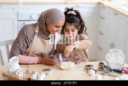 Petite fille arabe mignonne aidant son maman musulmane dans la cuisine, cuisant ensemble Banque D'Images