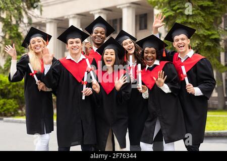 Divers étudiants internationaux avec diplômes célébrant la remise des diplômes, en agitant à la caméra Banque D'Images