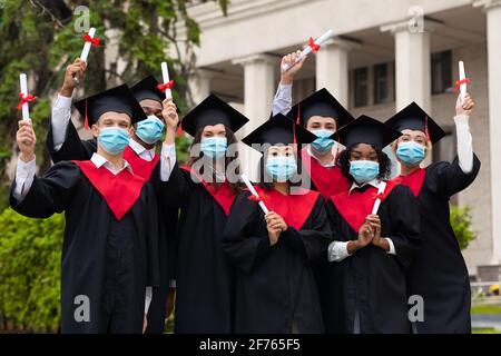 Divers étudiants internationaux en masques avec diplômes célébrant la graduation Banque D'Images