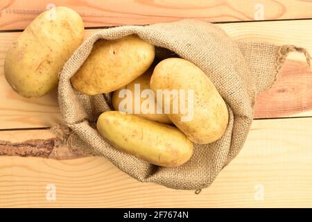 Plusieurs pommes de terre fraîches, non pelées, juteuses bio, dans un sac de jute, sur une table en bois. Banque D'Images