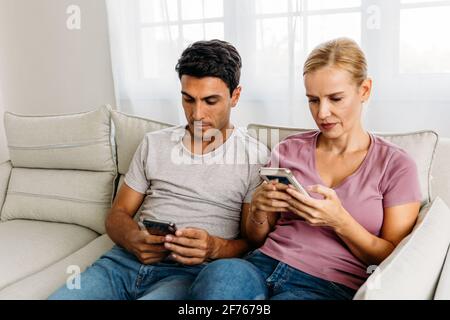 Un mari et une femme caucasiens très occupés se sont engarés dans leur propre mobile téléphone tout en naviguant sur les réseaux sociaux et en faisant des achats en ligne sur maison assise dans un canapé Banque D'Images