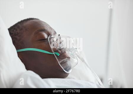 Portrait de vue latérale du jeune homme afro-américain dans le lit d'hôpital avec masque d'oxygène , copier l'espace Banque D'Images