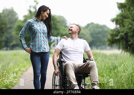 Un homme souriant en fauteuil roulant marche dans le parc avec une femme Banque D'Images