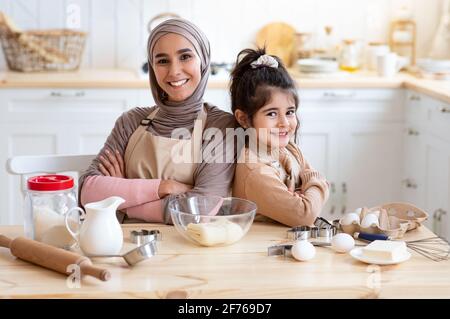 Bonne maman islamique et petite fille posant dans la cuisine pendant Cuisson en même temps Banque D'Images