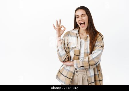 Oui, ça va. Souriante heureuse femme se moquant et montrant OK geste d'accord, insinuant tout est bien, tout est parfait, louant excellent choix, debout Banque D'Images