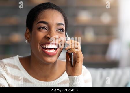 Gros plan de la joyeuse Afro-américaine féminine parlant sur le téléphone portable à Accueil Banque D'Images
