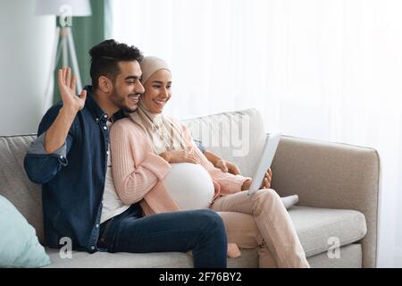 Joyeux futurs conjoints musulmans faisant des appels vidéo avec la tablette numérique À la maison Banque D'Images