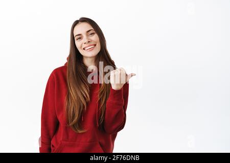 De cette façon. Souriante femme magnifique avec de longs cheveux pointant le pouce droit, montrant la publicité de côté sur l'espace de copie, de donner la recommandation, de louer le produit Banque D'Images