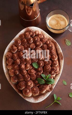 Tiramisu, dessert italien. Gâteau fait maison dans un plateau blanc avec biscuit au ladyfinger et crème mascarpone isolée sur fond marron. Directement au-dessus. Banque D'Images