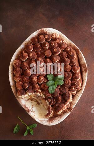 Tiramisu, dessert italien. Gâteau fait maison dans un plateau blanc avec biscuit au ladyfinger et crème mascarpone isolée sur fond marron. Directement au-dessus. Banque D'Images