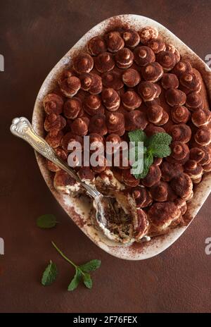 Tiramisu, dessert italien. Gâteau fait maison dans un plateau blanc avec biscuit au ladyfinger et crème mascarpone isolée sur fond marron. Directement au-dessus. Banque D'Images