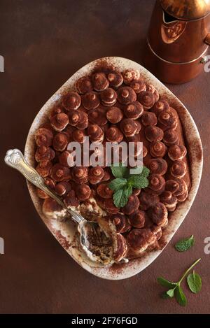 Tiramisu, dessert italien. Gâteau fait maison dans un plateau blanc avec biscuit au ladyfinger et crème mascarpone isolée sur fond marron. Directement au-dessus. Banque D'Images