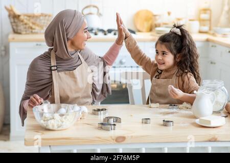 Maman arabe donnant High cinq à petite fille tout en cuisant Dans la cuisine Banque D'Images