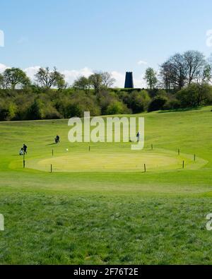 Vue sur un parc public et un parcours de golf avec des golfeurs et un moulin à l'horizon le matin de printemps à Beverley, dans le Yorkshire, au Royaume-Uni. Banque D'Images