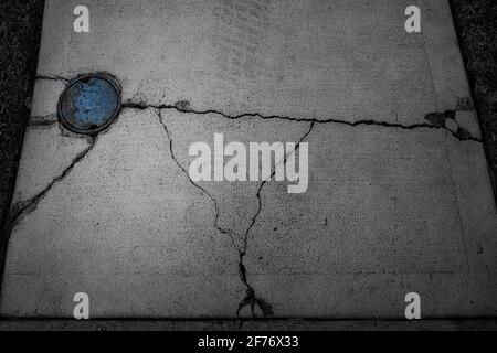 Abstrait, principalement photo en noir et blanc d'un trottoir en béton fissuré et brisé avec une couverture principale d'eau bleue. Banque D'Images