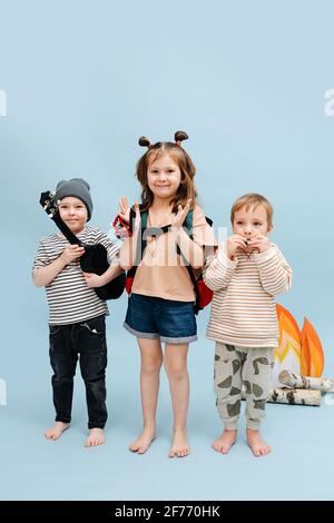 Des enfants à l'élévation se tenant près d'un faux feu de camp avec des flammes de papier et des bûches de bouleau. Ils posent pour une photo avec leurs instruments sur fond bleu Banque D'Images