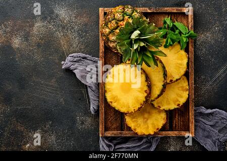 Émincé d'ananas mûr dans une boîte en bois sur fond de pierre brun foncé. Fruits tropicaux. Vue de dessus. Espace libre pour le texte. Maquette. Banque D'Images
