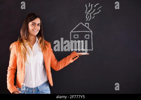 Bonne femme montrant un dessin de maison dans le tableau noir Banque D'Images