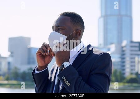 Un jeune homme d'affaires africain en costume bleu foncé élégant masque de protection en milieu urbain avant de rencontrer un partenaire ou collègue Banque D'Images