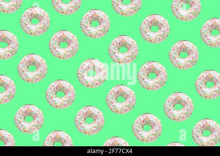 Motif composé de beignets en anneau avec glaçure blanche et de centaines et de milliers de courgeuses sur fond vert Banque D'Images