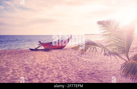 Petit bateau sur une plage vide au coucher du soleil, couleurs appliquées, Sri Lanka. Banque D'Images