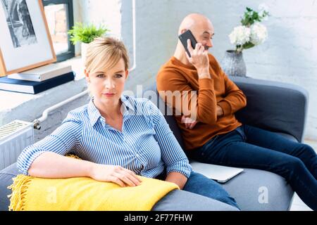 Prise de vue d'un couple d'âge moyen ignorant l'un l'autre après avoir un argument sur le canapé à la maison. Femme blonde assise sur le canapé pendant que son mari sitti Banque D'Images