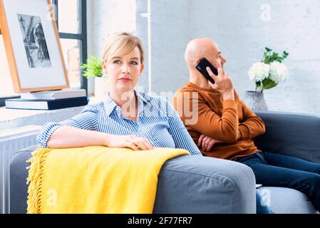 Prise de vue d'un couple d'âge moyen ignorant l'un l'autre après avoir un argument sur le canapé à la maison. Femme blonde assise sur le canapé pendant que son mari sitti Banque D'Images