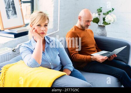 Prise de vue d'un couple d'âge moyen ignorant l'un l'autre après avoir un argument sur le canapé à la maison. Femme blonde assise sur le canapé pendant que son mari sitti Banque D'Images