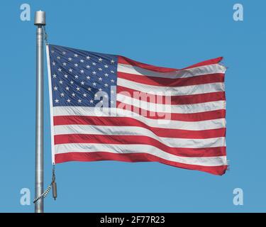 Gros plan sur un drapeau américain agitant dans un vent puissant sur le mât contre le ciel bleu clair Banque D'Images