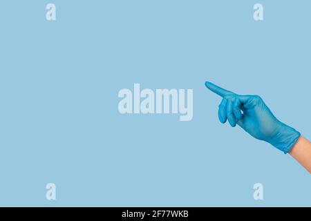 Main féminine dans un gant chirurgical médical bleu pointant sur quelque chose sur fond bleu clair Banque D'Images