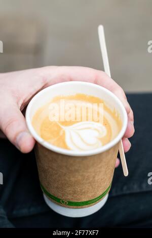Tasse de café recyclable tenue dans une main de l'homme caucasien avec une tige en bois, boisson savoureuse de caféine avec forme de coeur de crème dans le papier à usage unique Banque D'Images