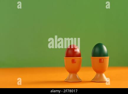 Deux œufs de pâques colorés peints dans des coquilles d'aubergines en gros plan fond vert et orange Banque D'Images