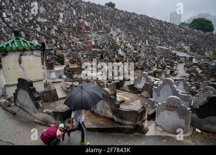 Un homme portant un parapluie marche à travers des pierres tombales dans un cimetière pendant le Ching Ming Festival à Hong Kong. Le Ching Ming Festival annuel, quand les gens visitent les tombes de parents décédés et quittent les lieux en souvenir et dans le respect que le gouvernement de Hong Kong tente de garder le nombre de cas infectés par le coronavirus COVID-19 sous contrôle tandis que davantage de personnes sont vaccinées. Banque D'Images