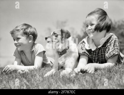 GARÇON ET FILLE SOURIANTE DES ANNÉES 1930 UN FRÈRE ET UNE SŒUR MENTANT ENSEMBLE DANS L'HERBE AVEC LEUR CHIEN ENTRE - D4419 HAR001 HARS FEMMES FRÈRES RURAUX SAINTETÉ VIE À LA MAISON COPIE ESPACE AMITIÉ HOMMES ANIMAUX SOLEIL SÉRÉNITÉ FRÈRES ET SŒURS CONFIANCE SŒURS B&W. ÉTÉ BONHEUR MAMMIFÈRES TÊTE ET ÉPAULES GAIES ET CANINES BAS ANGLE FRÈRE SOURIT COOCH CONNEXION CONCEPTUELLE JOYEUSE MUTT CROISSANCE CANINE JUVÉNILES SAISON DES MAMMIFÈRES PRINTEMPS TOGETHERNESS NOIR ET BLANC RACE BLANCHE HAR001 À CÔTÉ MIXTE RACE ANCIENNE Banque D'Images