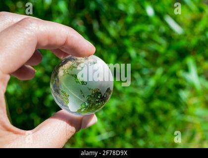 Globe de cristal dans la main d'un homme contre un fond de feuillage vert. Concept de protection de la terre. Jour de la Terre Banque D'Images