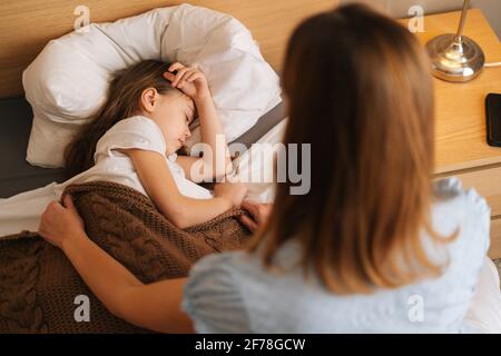 Vue en haut à l'arrière de l'adorable petite fille malade dormant sur le lit dans la chambre des enfants sous la couverture à la maison. Banque D'Images